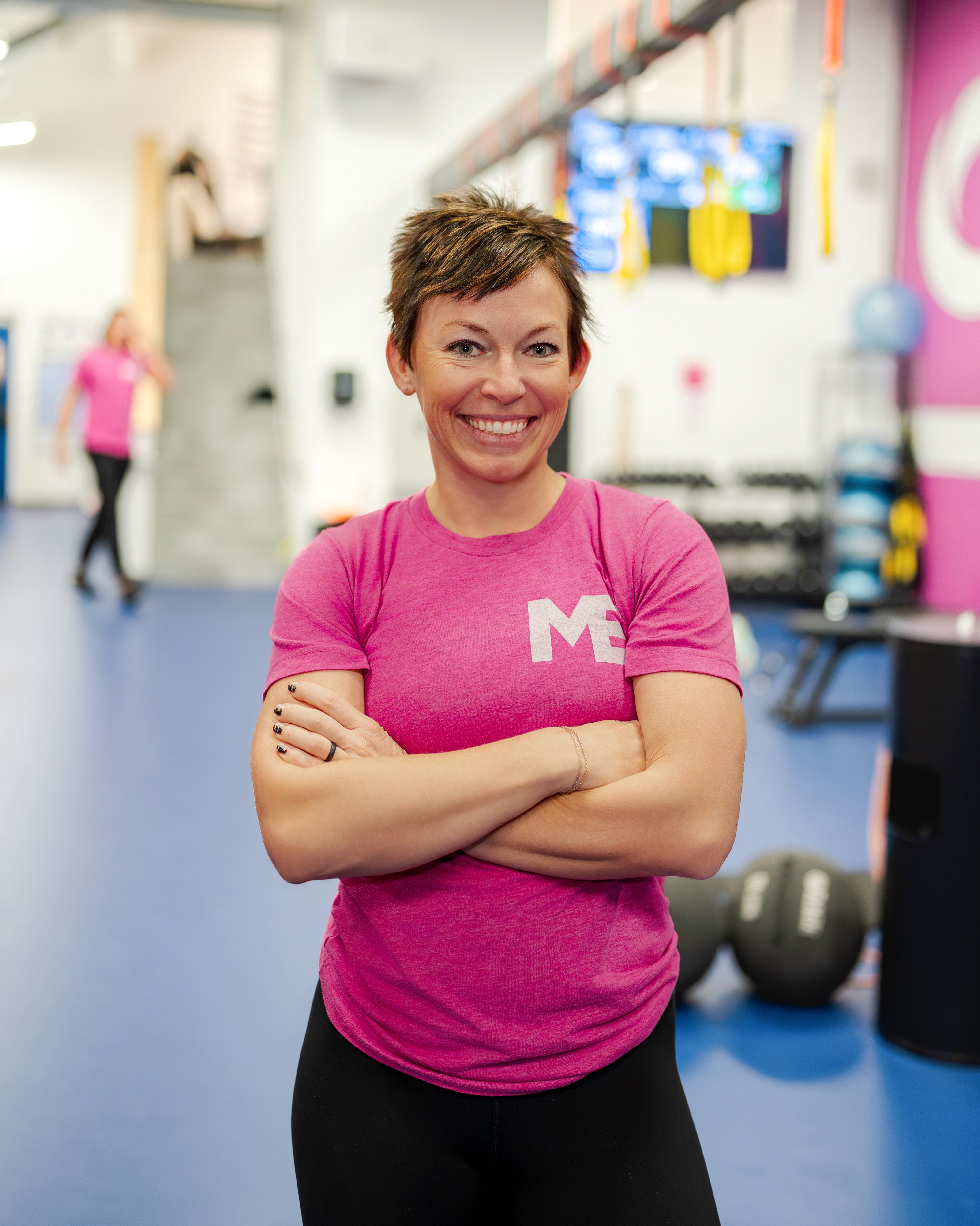 Megan Cooper, owner and head coach of Studio ME Fitness, standing with arms crossed and smiling in her Northeast Minneapolis strength studio.